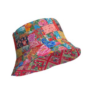 Op de afbeelding: Een kleurrijke patchwork-emmerhoed met verschillende bloempatronen in rood, roze, blauw, geel en groen. De hoed heeft een brede rand en een afgeronde kroon, met een levendig, opvallend ontwerp.