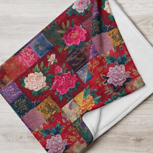 Pode incluir: Uma manta vermelha com um design de patchwork com padrões florais e várias texturas. A manta apresenta grandes peónias rosa, brancas e amarelas. A parte inferior da manta é branca.