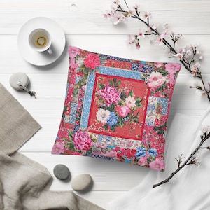 May include: Square decorative pillow with a floral design. The pillow features a red center with a bouquet of pink, white, and blue flowers. The border is a patchwork of floral patterns in shades of pink, blue, and red.