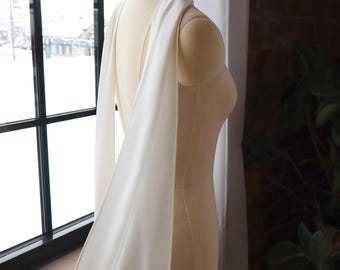 May include: A white satin shawl draped over a dress form. The shawl is long and flowing, with a simple design.
