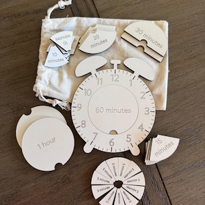 May include: A white wooden clock puzzle with various time increments. Includes pieces labelled "10 minutes", "20 minutes", "30 minutes", "1 hour", and "15 minutes". A small bag holds some of the pieces. The clock face is labelled "60 minutes".