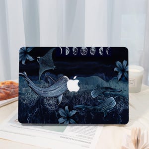 Könnte beinhalten: Eine Laptop-Hülle mit einer dunkelblauen Unterwasserszene, Walhaien, einem Mantarochen und Blumenmotiven. Oben ist eine Reihe von Mondphasen abgebildet. Das Design integriert das weiße Apple-Logo als Aussparung in der Mitte des Haupthais.