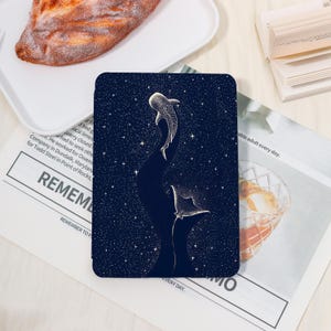 May include: A dark blue tablet case with a starry night design and two stylized whale sharks in white. The illustration has a celestial theme. The text "REMEMBER TO" is visible on the newspaper.