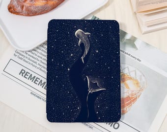 May include: A dark blue tablet case featuring a starry night design with two stylized whale sharks. The illustration is in white and has a celestial theme. The text "REMEMBER TO" is visible on the newspaper.