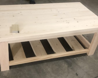 May include: A light wood coffee table with a rectangular top and a lower shelf with four slats. The table is made of unfinished wood and has a natural wood grain.
