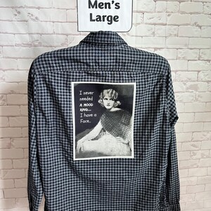 May include: A black and gray plaid button-down shirt with a rectangular graphic on the back. The graphic features a black and white image of a woman and the text: "I never needed a mood ring... I have a Face..." A white sign above the shirt reads "Men's Large."