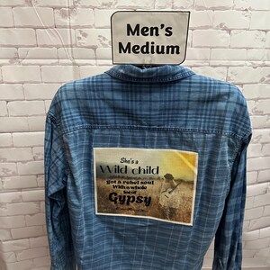 May include: A blue plaid button-down shirt with a patch on the back that says "She's a Wild child got a rebel soul With a whole lot of Gypsy".