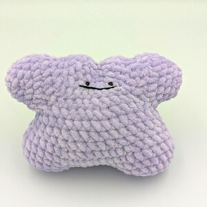 May include: A plush purple crocheted toy shaped like a star with a simple black face.