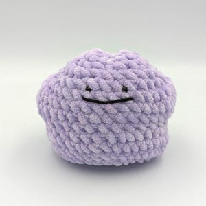 May include: A purple crocheted plush toy shaped like a ghost with a black embroidered smile.