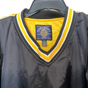 May include: Black windbreaker jacket with yellow and white stripes on the collar. The jacket has a v-neck and a label that reads "Steve & Barry's Outfitters".