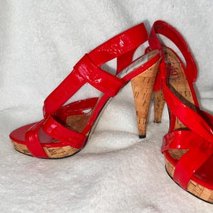 Puede incluir: Un par de sandalias rojas de tacón alto con cuñas de corcho y un diseño de tiras cruzadas.
