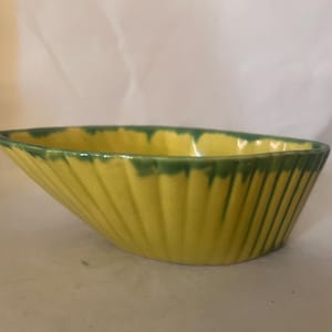 以下が含まれることがあります： ボートのような形の黄色のセラミックボウル。ボウルはリブ加工された外側と、縁に沿った緑色のトリムが付いています。ボウルの長さは約20cm、幅は約10cmです。