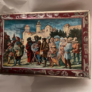 May include: Rectangular metal box with a claret frame and a detailed illustration. The illustration shows a group of people in historical attire in front of a castle. The box has a silver trim and a decorative border.
