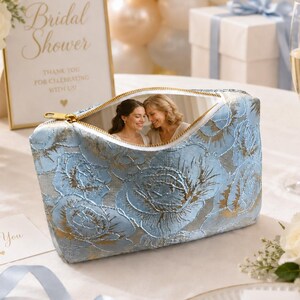 May include: A light blue cosmetic bag with a gold zipper and a floral pattern. The bag is open, revealing a photo of two women. A framed sign reads "Bridal Shower".