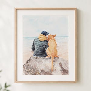 Op de afbeelding: Waterverfprint van een persoon en een golden retriever hond die op een rots op het strand zitten. De persoon draagt een blauwe pet, gele hoodie en een donker gewatteerde jas. De hond is lichtbruin van kleur.