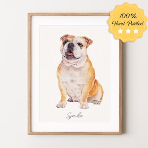 May include: A watercolor painting of a bulldog sitting. The dog is brown and white with a pink nose. The painting is framed in a light wood frame. The dog's name, "Spike", is written in cursive at the bottom of the painting.