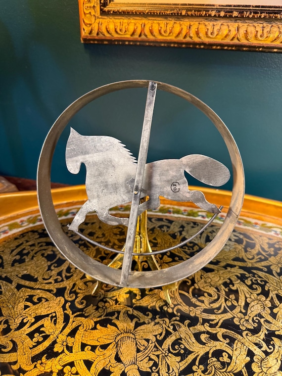A steel horse in motion, frozen mid-gallop on a brass easel — old-school kinetic sculpture craft that looks like it belongs in a ranch study.