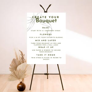 May include: A white sign on a black easel with instructions on how to create a bouquet. The sign reads "Create Your Bouquet" with steps for base, flowers, mix and layer, wrap it up, and take it home. A vase with dried flowers is in the foreground.