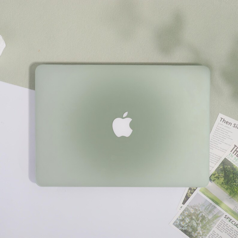 May include: A pale green Apple laptop with the Apple logo in the centre. The laptop is on a white and light green surface. The laptop is closed. There are some printed papers to the right of the laptop.