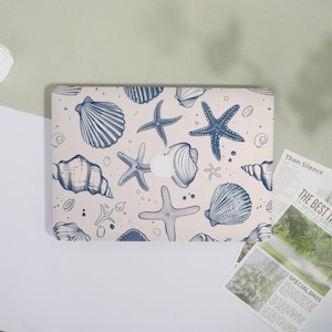May include: A laptop case with a cream backdrop, adorned with a pattern of blue seashells and starfish. The design showcases diverse marine life forms, evoking a seaside theme. The case incorporates a cutout for the Apple logo.