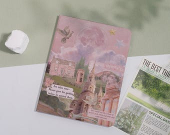 May include: A pink journal with a collage design featuring a dove, a full moon, stars, and a castle. Text on the journal reads "Art takes time - Monet grew his gardens before he painted them." A newspaper is partially visible.