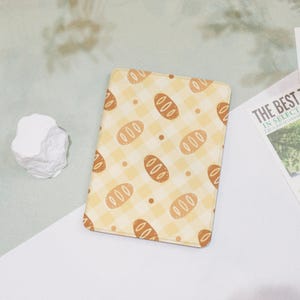 May include: A yellow and brown patterned fabric wallet with a repeating pattern of bread loaves. The fabric has a checkered pattern.