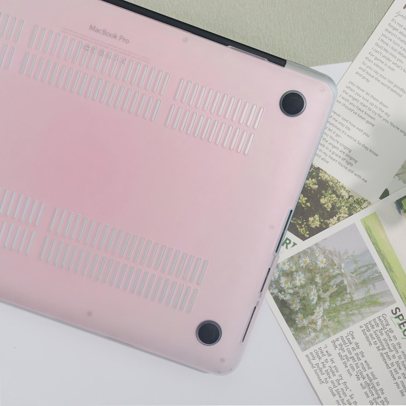 May include: A light pink MacBook Pro case with ventilation slots and black rubber feet. The case has the words "MacBook Pro" printed on it. The case is designed to protect the laptop.