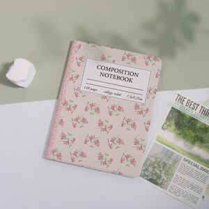 May include: A composition notebook with a floral pattern and the text "COMPOSITION NOTEBOOK". The notebook is 7.5x9.25 inches and has 110 college-ruled pages. The cover is light pink with a pink floral design.