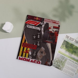 May include: A notebook with a Formula 1 racing theme. The cover features a collage with the word "Ferrari" and the text "Drive fast" in a red and white design. The word "Monaco" is also visible.