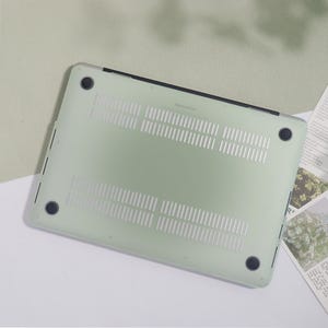 May include: A pale green MacBook Pro case with a transparent design. The case features ventilation slots and four black rubber feet. The case is designed to protect the laptop from scratches and other damage.