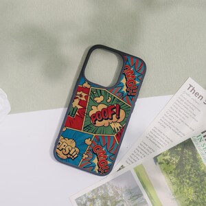 May include: A phone case with a comic book design. The case features a black border and a colorful pattern with the words "POOF!", "OMG!!", and "OPS!!" in speech bubbles. The background is a mix of red, blue, and green.