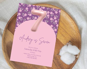 May include: A pink and purple invitation card with a large pink number seven balloon. The text on the card reads "Audrey is Seven" and includes details for a birthday party.