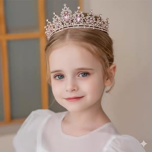 May include: A rose gold tiara with clear and pink crystals. The crown features a series of sparkling clear crystals and larger pink gems. The tiara is designed with an ornate, elegant style, perfect for special occasions.
