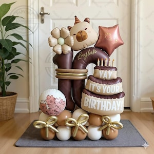 Könnte beinhalten: Eine festliche Geburtstagsballon-Anordnung mit einer großen Eins, einem bärenförmigen Ballon, einem sternförmigen Ballon und einem kuchenförmigen Ballon mit dem Text "Yay It's Your Birthday!". Die Anordnung umfasst einen Blumenballon und einen Ballon mit Bärenillustrationen.