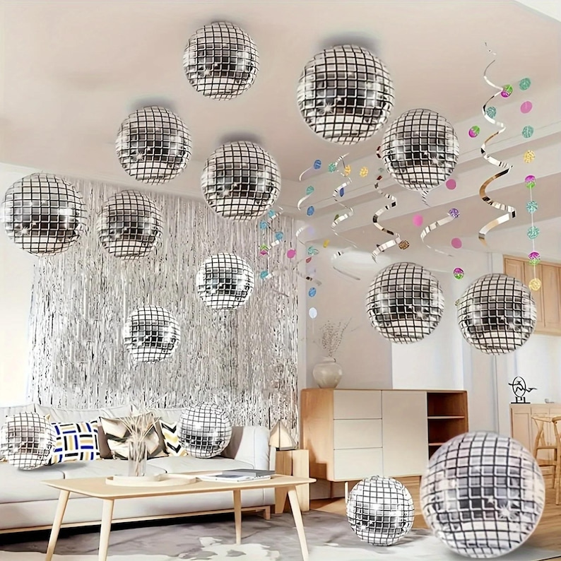 May include: A room decorated with multiple silver disco balls of varying sizes, hanging from the ceiling. Silver fringe and colorful streamers add to the festive atmosphere. A sofa and wooden furniture are visible in the background.