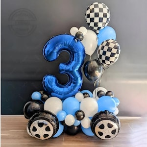 May include: A celebratory balloon display with a large blue number 3 balloon, black and white chequered balloons, and a collection of blue, white, and black balloons. Two wheel-shaped balloons complete the race car theme.