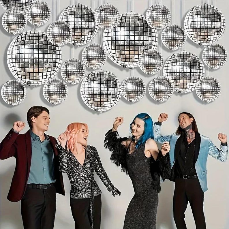 May include: A group of people dancing in front of a wall decorated with silver disco balls. The disco balls are round and reflective, with a grid-like pattern. The people are wearing various outfits, including a maroon blazer, a black dress, and a light blue jacket.