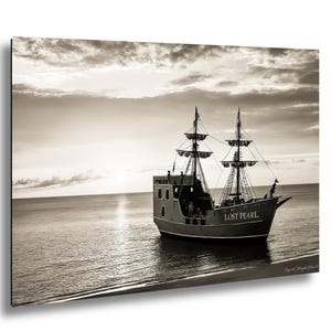 May include: Sepia photograph of a pirate ship, the "Lost Pearl," on the sea. The ship has two masts with rigging and sails, and the name is visible on the bow. The sky is cloudy, and the ship is near the shore.