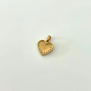 K&ouml;nnte beinhalten: Goldfarbener Herzanh&auml;nger mit &Ouml;se. Das Herz ist mit kleinen, klaren Edelsteinen umrandet. Der Anh&auml;nger ist wahrscheinlich aus Gold gefertigt und als Schmuckst&uuml;ck zum Tragen gedacht.