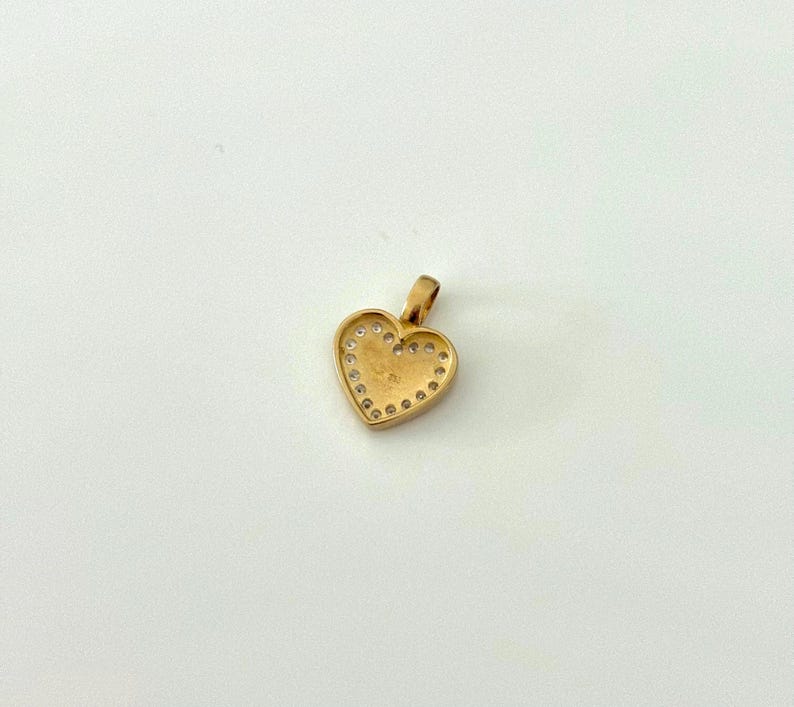K&ouml;nnte beinhalten: Goldfarbener Herzanh&auml;nger mit &Ouml;se. Das Herz ist mit kleinen, klaren Edelsteinen umrandet. Der Anh&auml;nger ist wahrscheinlich aus Gold gefertigt und als Schmuckst&uuml;ck zum Tragen gedacht.