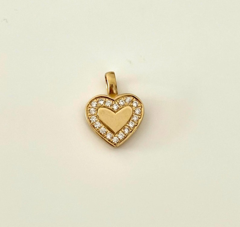 K&ouml;nnte beinhalten: Goldfarbener herzf&ouml;rmiger Anh&auml;nger mit einem Kranz aus kleinen, klaren Edelsteinen, die das innere Herz umgeben. Der Anh&auml;nger hat eine kleine Schlaufe f&uuml;r eine Kette. Ein klassisches Symbol f&uuml;r Liebe und Zuneigung.