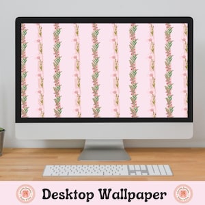 May include: A desktop computer displaying a pink floral wallpaper with a repeating pattern of green leaves and pink flowers. The computer is on a wooden desk with a cactus plant in a pot and a stack of books to the right.