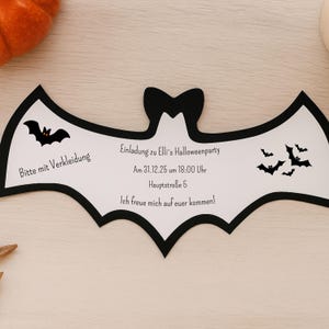 Könnte beinhalten: Eine Halloween-Party-Einladung in Form einer Fledermaus. Die weiße Karte hat einen schwarzen Rand und enthält den Text "Bitte mit Verkleidung" und "Einladung zu Elli's Halloweenparty". Mehrere Fledermaus-Silhouetten sind ebenfalls abgebildet.