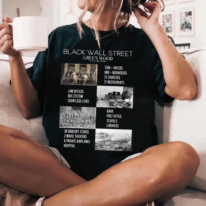 May include: Black t-shirt with a graphic print of a historical neighborhood called "Black Wall Street" in Greenwood, Oklahoma. The graphic includes text and images of the neighborhood's history, including the number of houses, businesses, churches, and restaurants.
