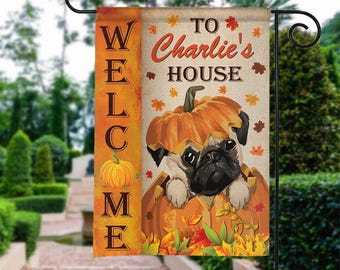 May include: A decorative garden flag with a pug dog emerging from a pumpkin. The flag reads "WELCOME" and "TO Charlie's HOUSE" with autumn leaves. The flag is orange, brown, and beige.