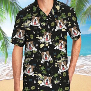 May include: A black short-sleeve button-down shirt featuring a repeating pattern of brown and white bulldog faces with tongues out, interspersed with green palm trees, small white sailboats, and yellow suns against a dark background.