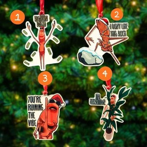 May include: Four Christmas tree ornaments with red ribbons. Each ornament features a cartoon character with text: "RIGATONI PASTA", "I DON'T LIKE THIS ROCK", "YOU'RE RUINING THE VIBE", and "I'M SENSITIVE". The ornaments are on a green Christmas tree.