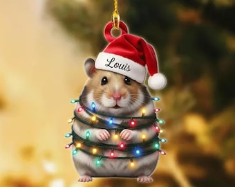May include: A Christmas ornament featuring a hamster wearing a Santa hat with the name "Louis" and wrapped in a string of colorful Christmas lights. The ornament is designed to hang and is set against a blurred background.
