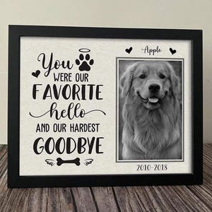 May include: A black framed memorial picture with a grayscale photo of a Golden Retriever dog named Apple. The text reads "You were our favorite hello and our hardest goodbye" with the years 2010-2018 below the photo.