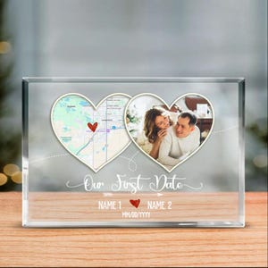 May include: A clear glass block with a photo of a couple in a heart-shaped frame. The left heart contains a map with a red heart marker. The text "Our First Date" and names are below the photo.